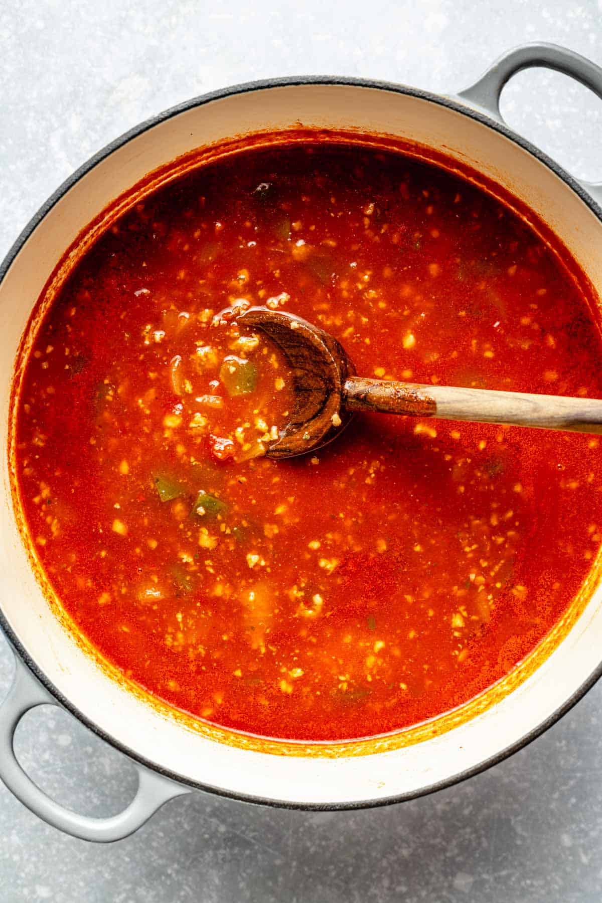 tomato liquid added to a large dutch oven with a wooden spoon