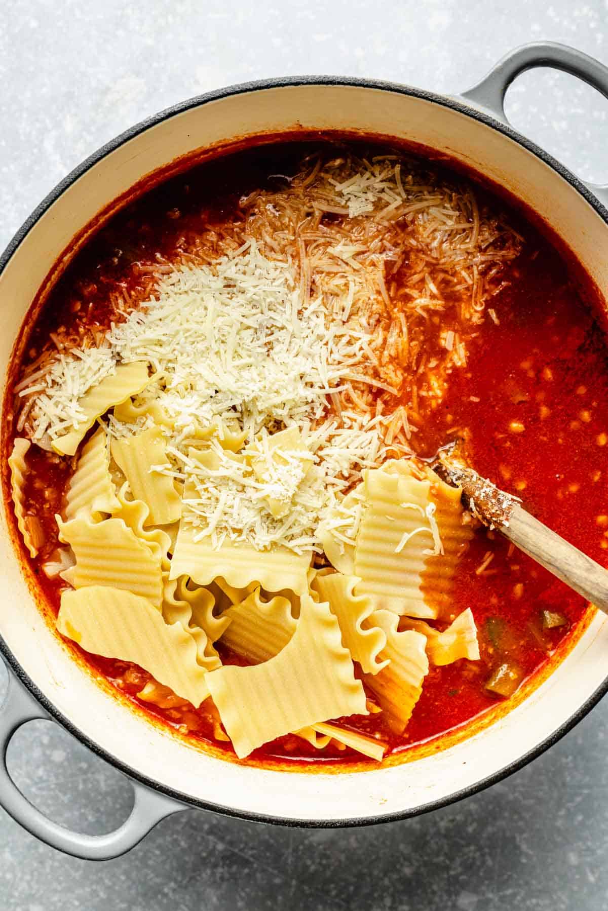 broken lasagna noodles and parmesan cheese added to the pot of soup