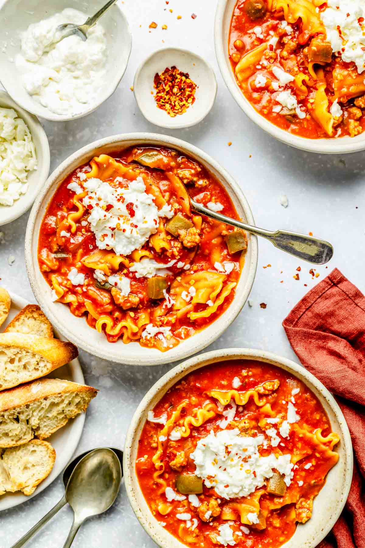 three bowls of lasagna soup with ricotta topping next to toasted bread