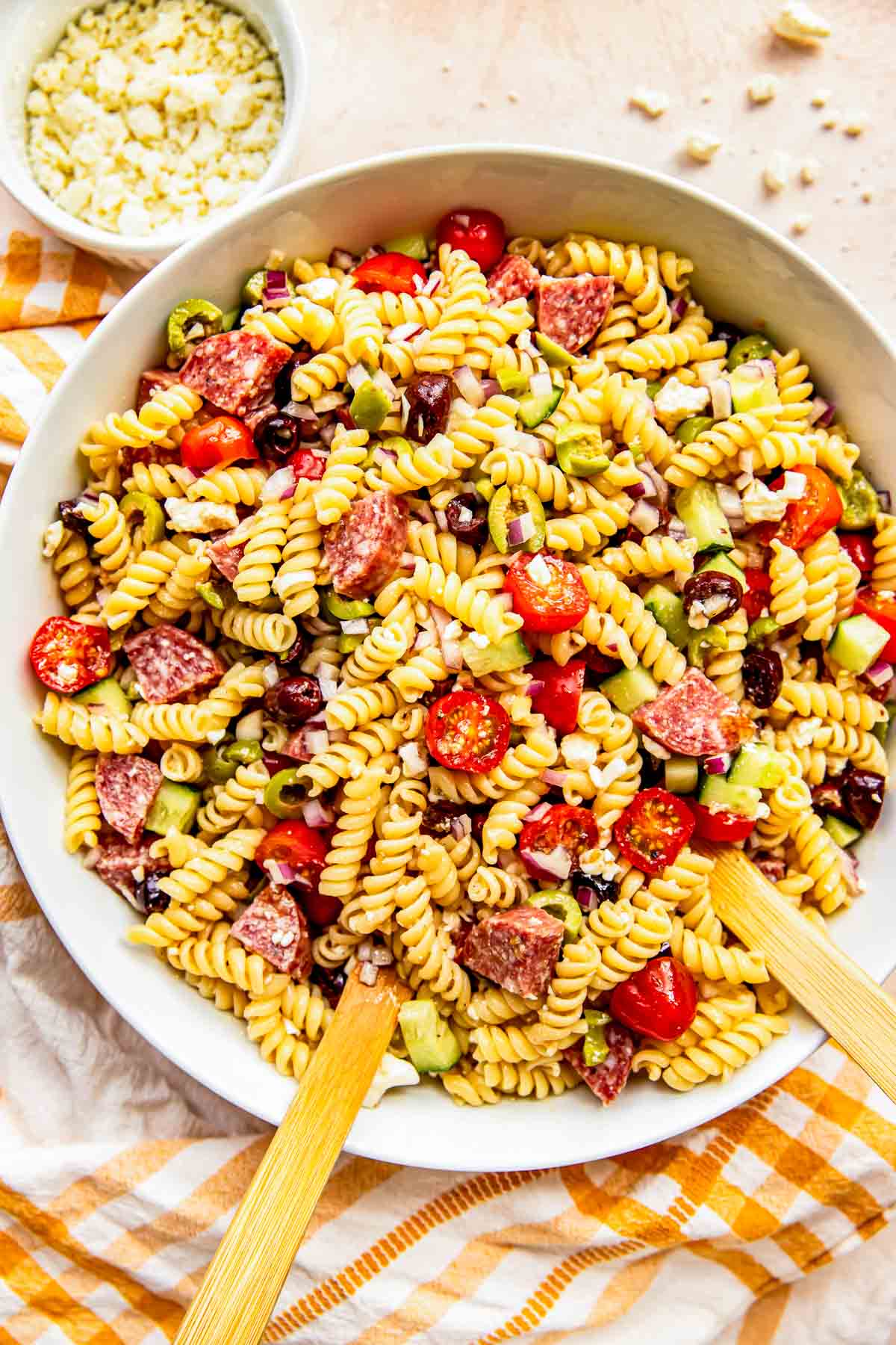 mediterranean pasta salad in a large white bowl with wooden spoons next to a bowl of feta