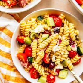 mediterranean pasta salad in a white bowl next to a gingham yellow towel