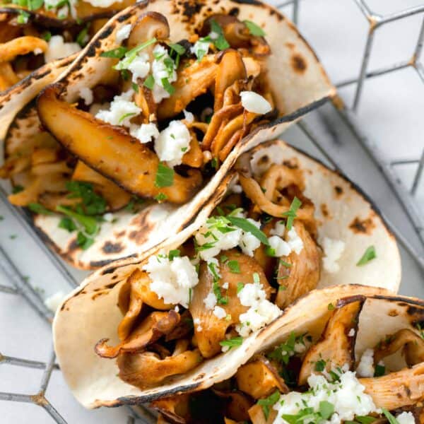 oyster mushroom tacos stacked in a wire basket with fresh parsley and cotija cheese garnished on top