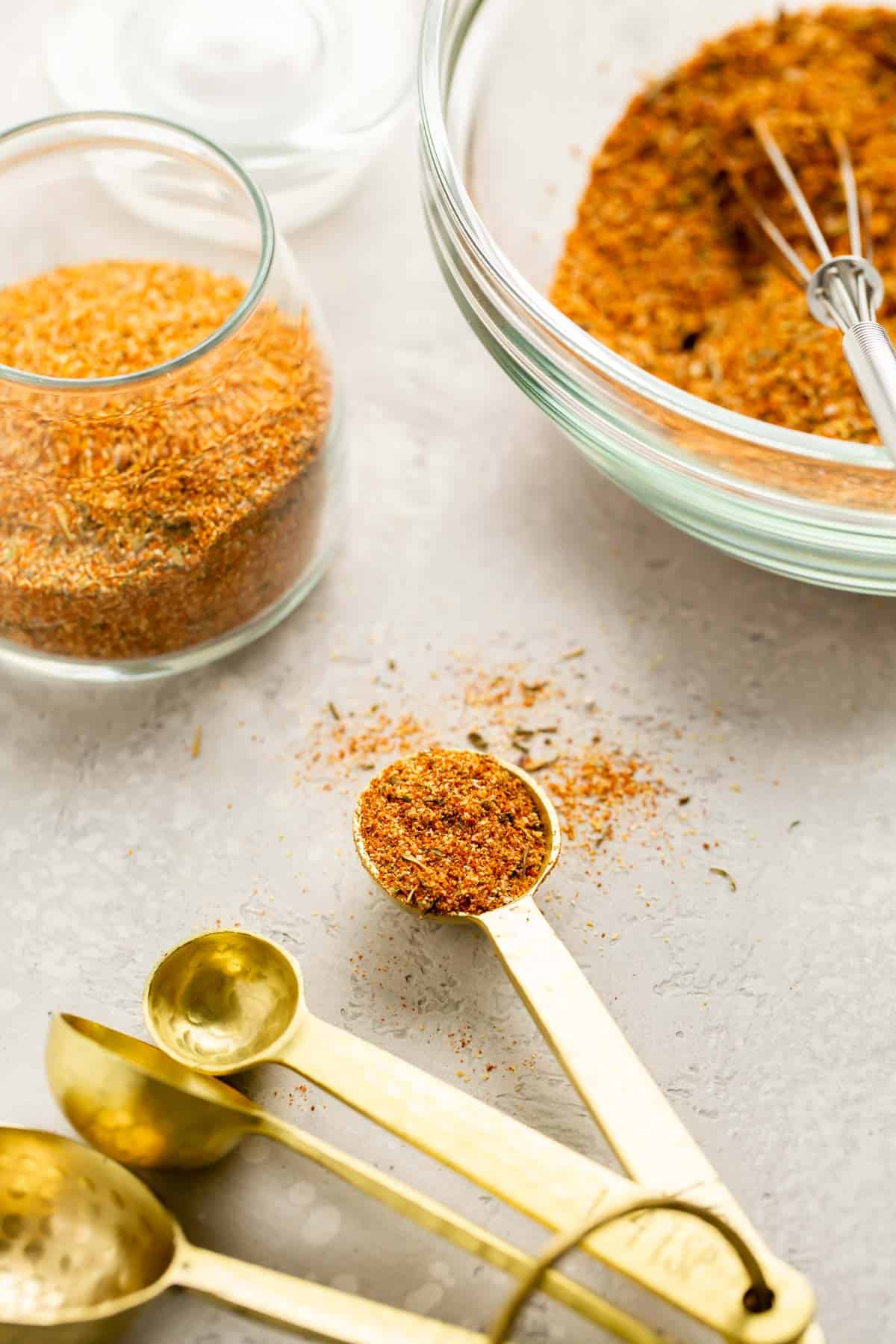 seafood seasoning on a gold teaspoon next to glasses of other seafood seasoning mix