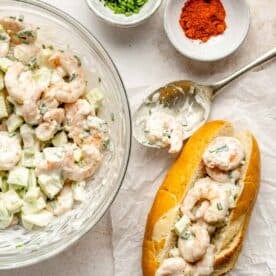 shrimp roll ingredients mixed together with a metal spoon laying next to an assembled shrimp roll