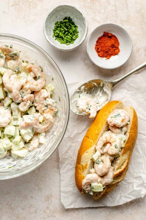 shrimp roll ingredients mixed together with a metal spoon laying next to an assembled shrimp roll