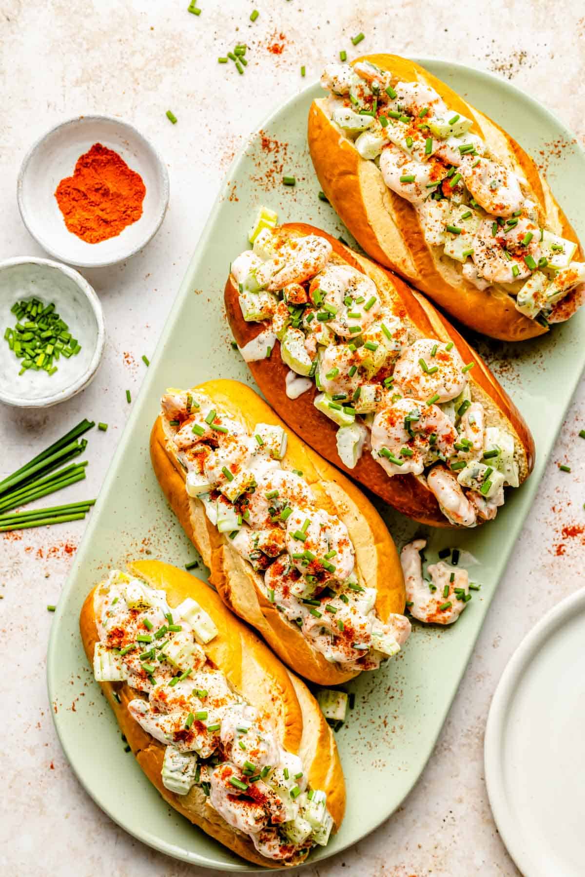 4 shrimp rolls lined up on a green plate next to fresh chives