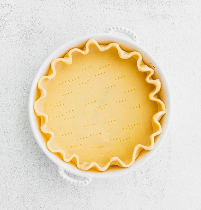 raw dough in a pie dish with fork piercings in the dough