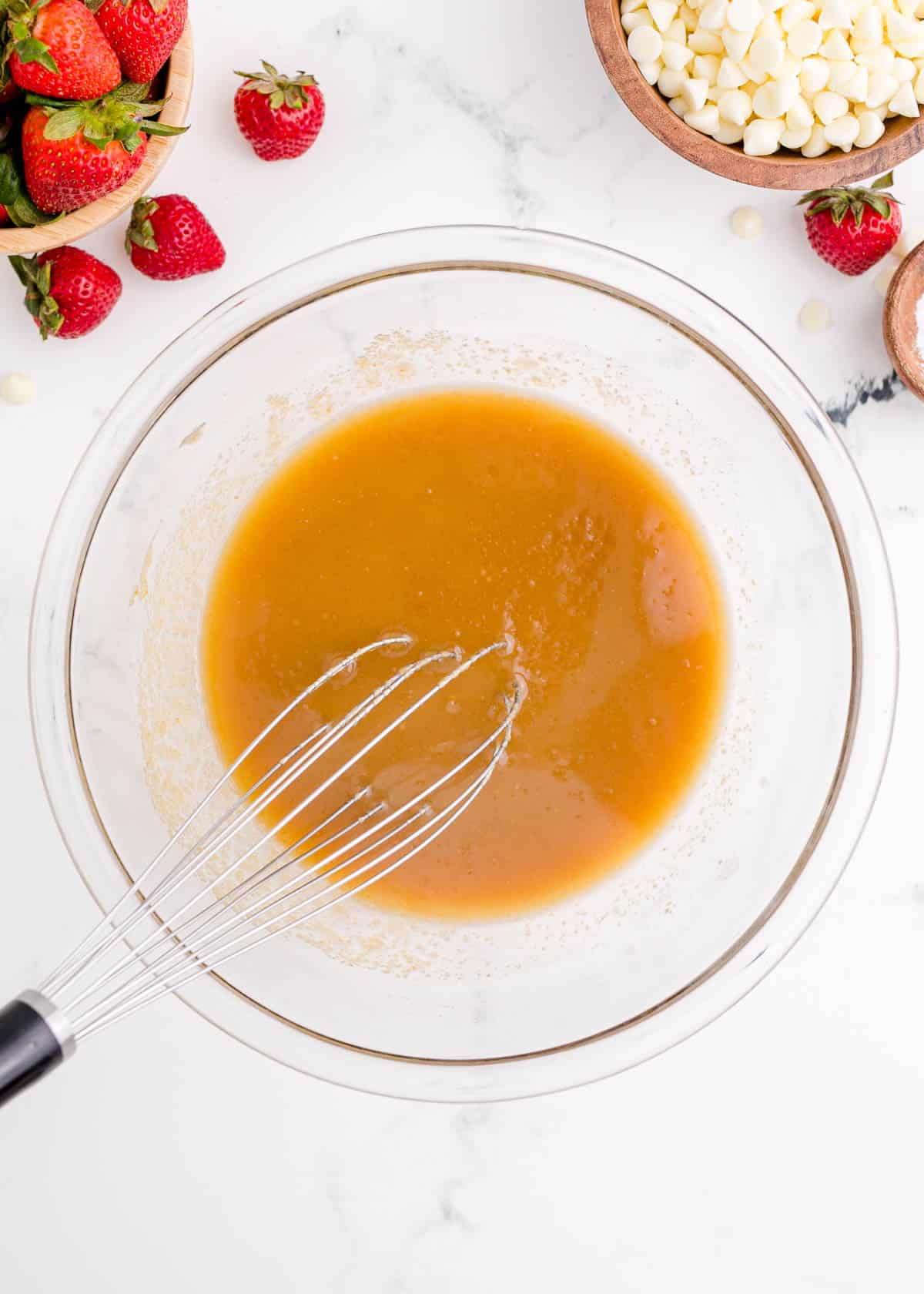 butter, brown sugar, vanilla, and eggs mixed together in a clear glass bowl with a metal whisk