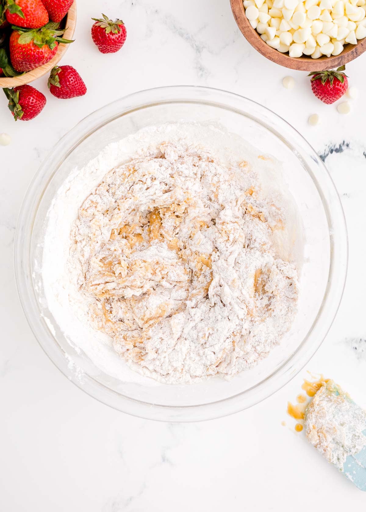 dry ingredients mixed into wet ingredients in a clear glass bowl next to fresh strawberries