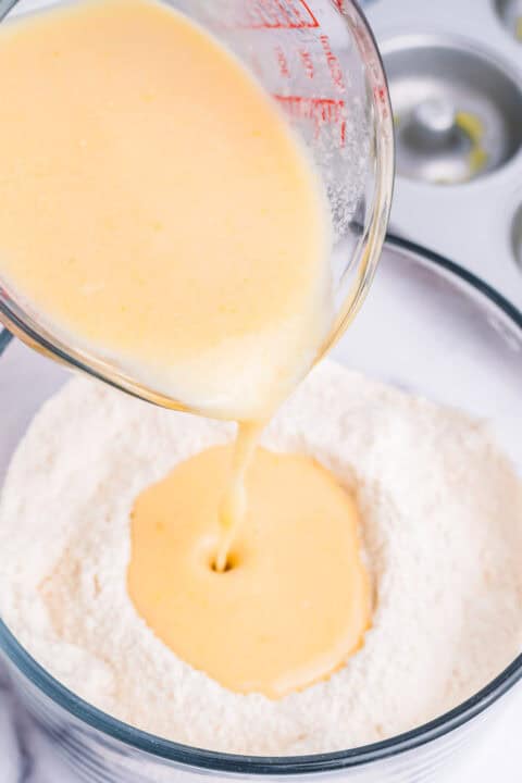 wet ingredients from a measuring cup being poured into a bowl of dry ingredients