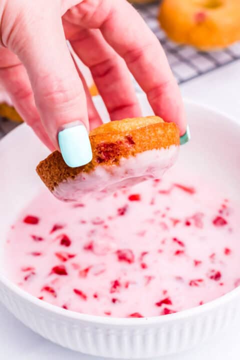 a cooled strawberry donut is being dipped into the strawberry glaze