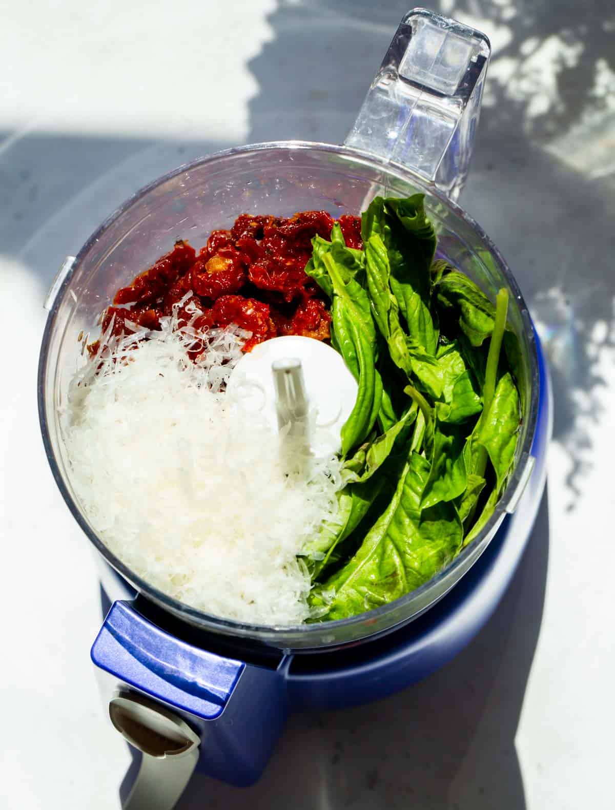 fresh basil, sun-dried tomatoes, and parmesan cheese in the bowl of a food processor