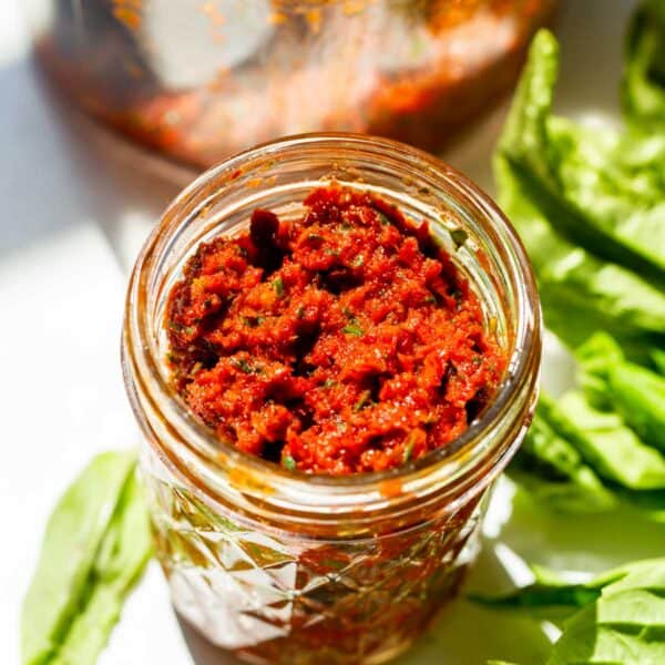 sun-dried tomato pesto in a glass mason jar next to fresh basil