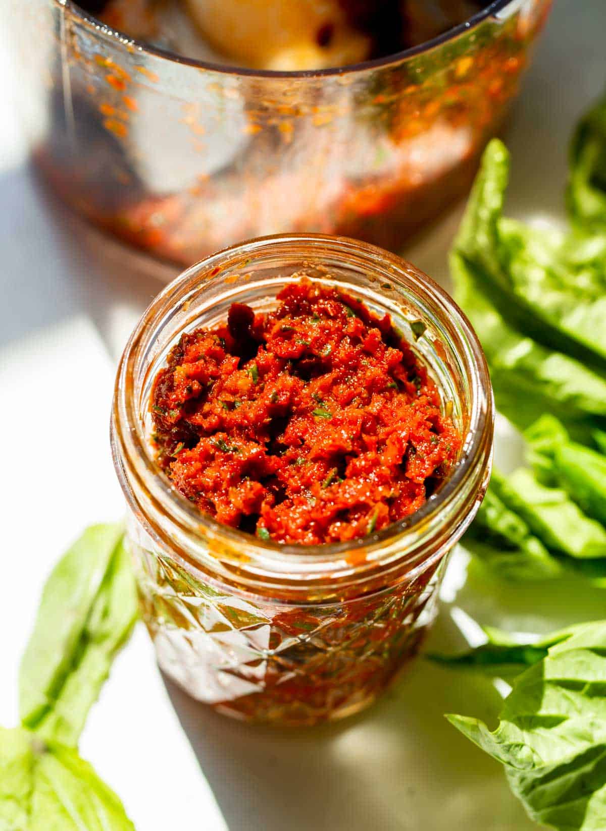 sun-dried tomato pesto in a glass mason jar next to fresh basil