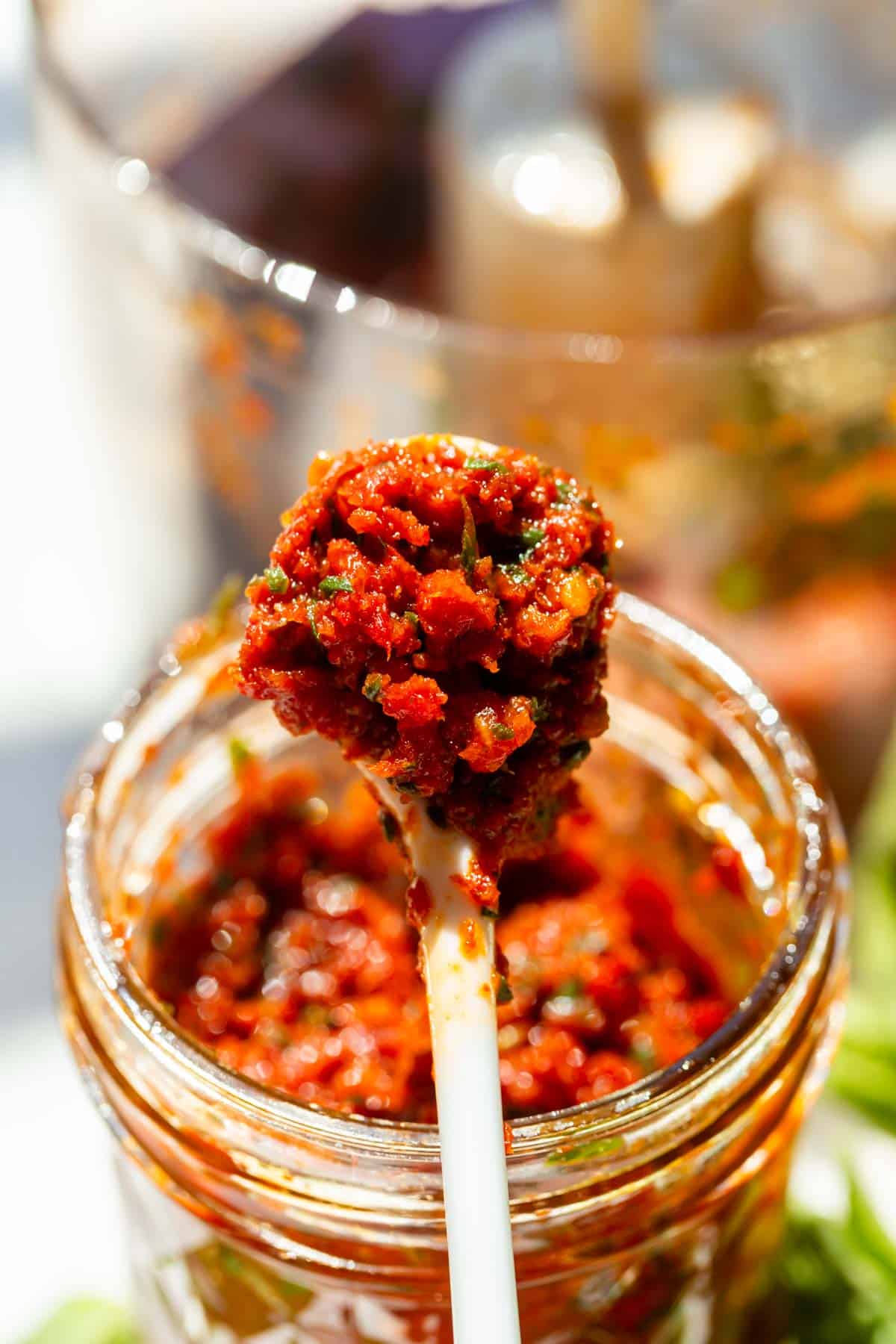 sun-dried tomato pesto is on a white spoon being lifted out of the glass jar