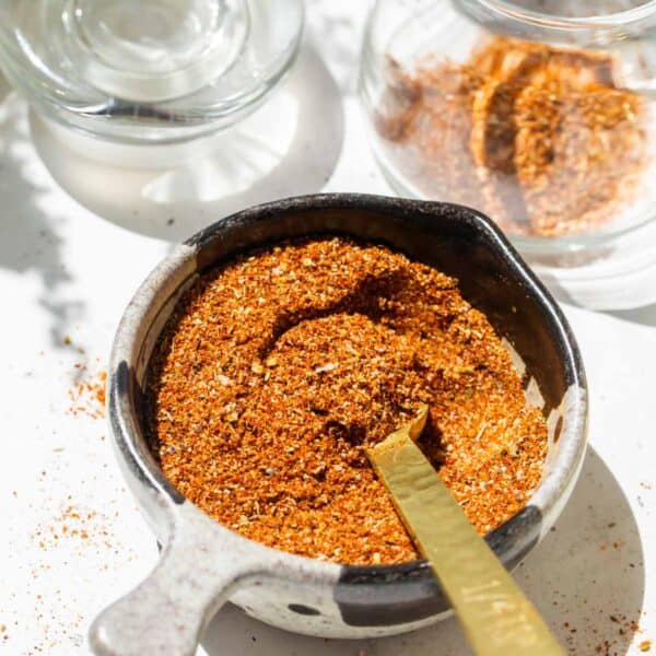 a gold measuring spoon in a measuring cup filled with taco seasoning next to a glass jar