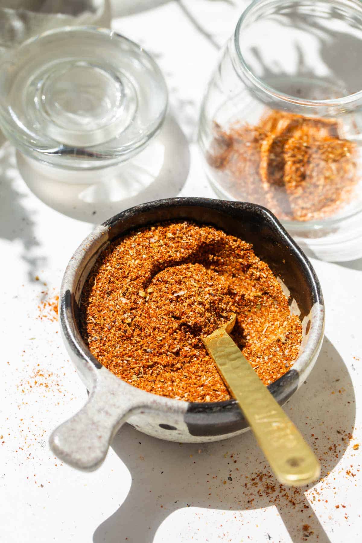 a gold measuring spoon in a measuring cup filled with taco seasoning next to a glass jar