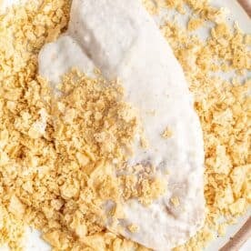 tilapia coated in batter being dipped into a plate of crushed tortilla chips