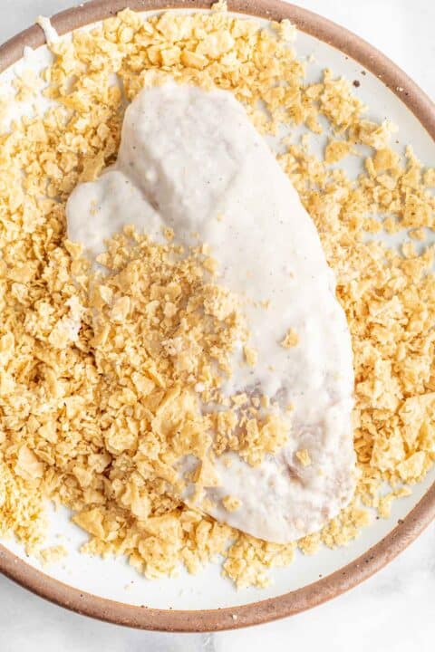 tilapia coated in batter being dipped into a plate of crushed tortilla chips
