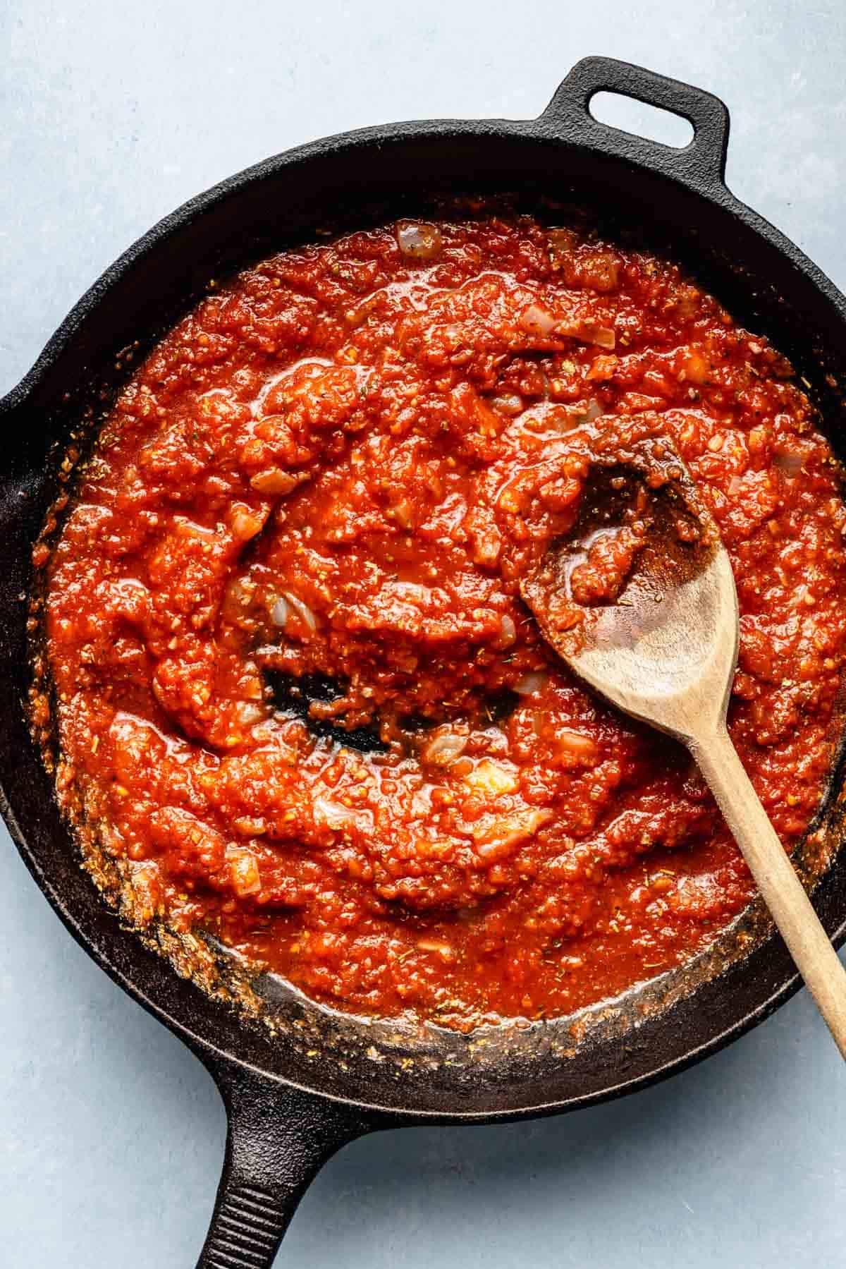 tomato sauce in a cast iron skillet with a wooden spoon