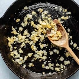 onions and garlic sautéed in a cast iron skillet with a wooden spoon