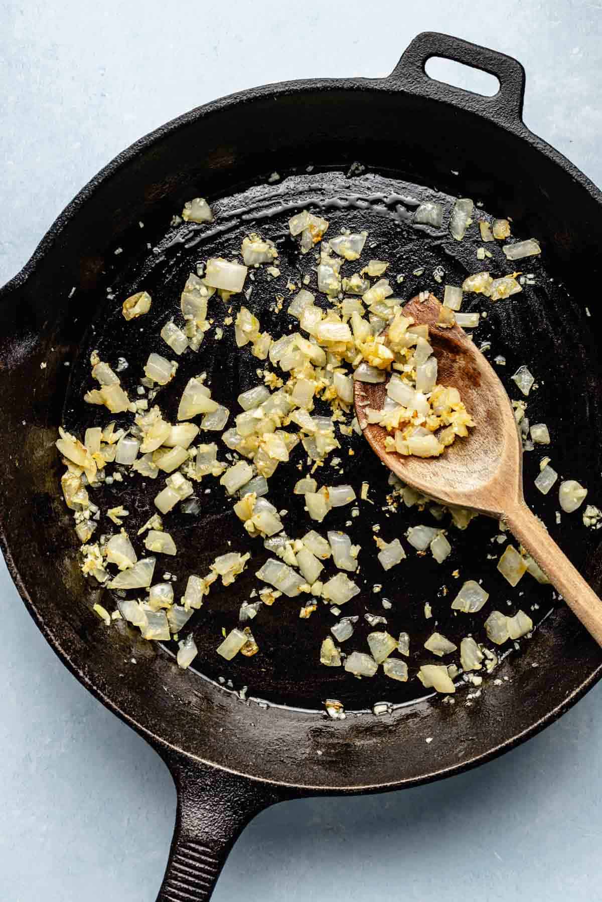 onions and garlic sautéed in a cast iron skillet with a wooden spoon