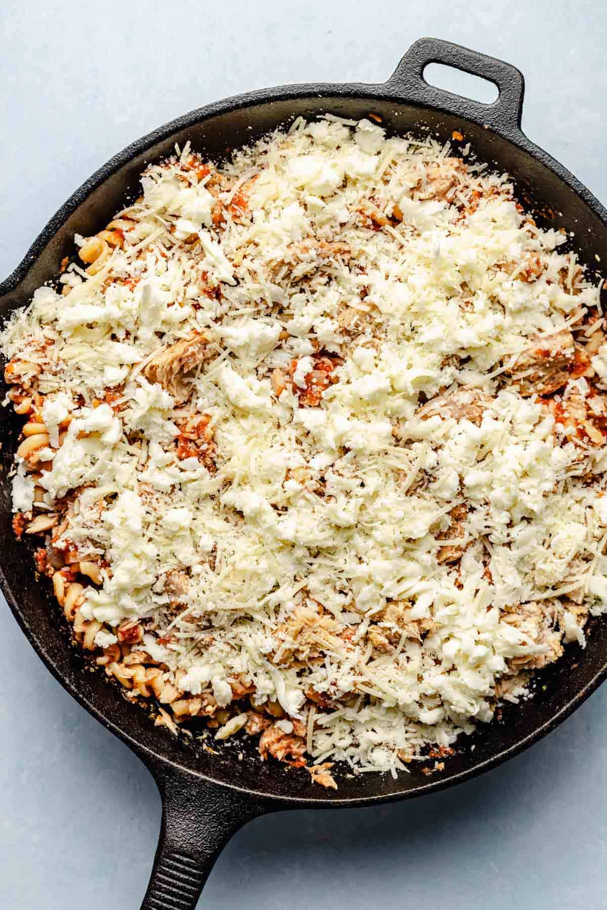 shredded mozzarella cheese and parmesan cheese sprinkled on top of pasta in cast iron skillet