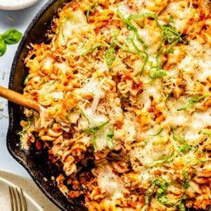 a wooden spoon scoops out a portion of tuna pasta bake in the cast iron skillet