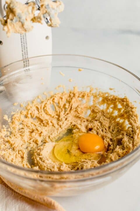 an egg is on top of the butter and sugar mixture with a hand mixer next to the clear bowl