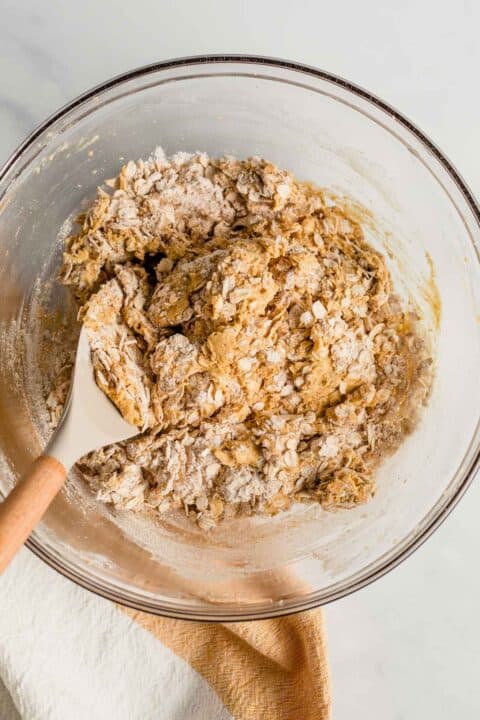 old fashioned oats are being folded into the cookie dough with a silicone spoon