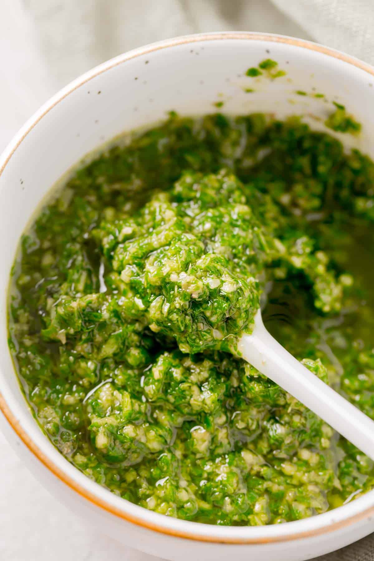 a white spoon has basil pesto on top in a gold rimmed bowl