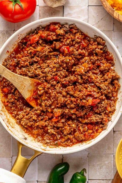 ground beef mixture mixed with red enchilada sauce in a white skillet with a wooden spoon in the center