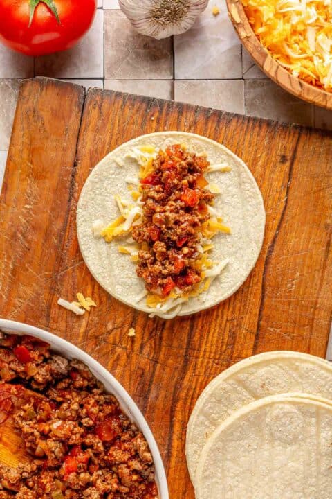 a corn tortilla with shredded cheese and ground beef mixture in the center