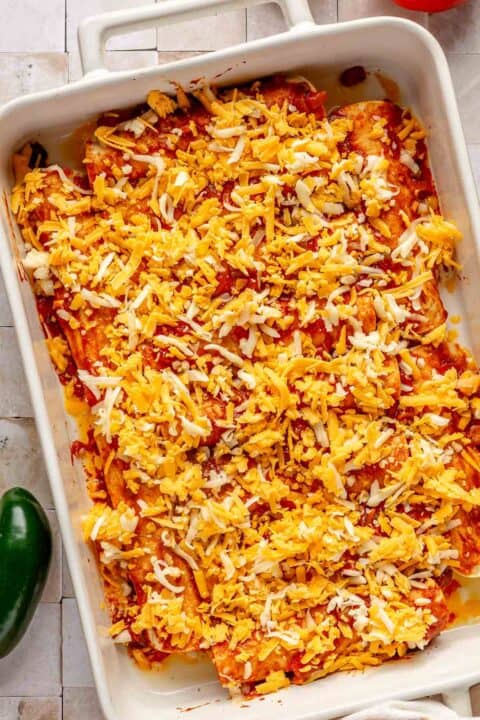 beef enchiladas in a baking dish with red enchilada sauce and shredded cheese sprinkled on top