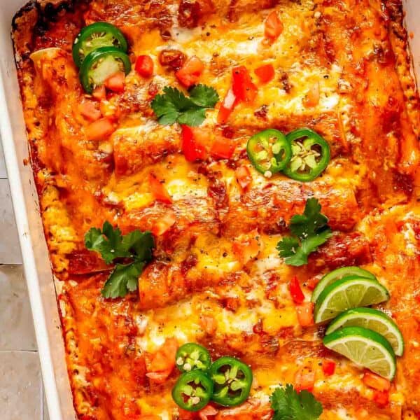 beef enchiladas in a baking dish topped with cilantro, jalapeños and lime slices