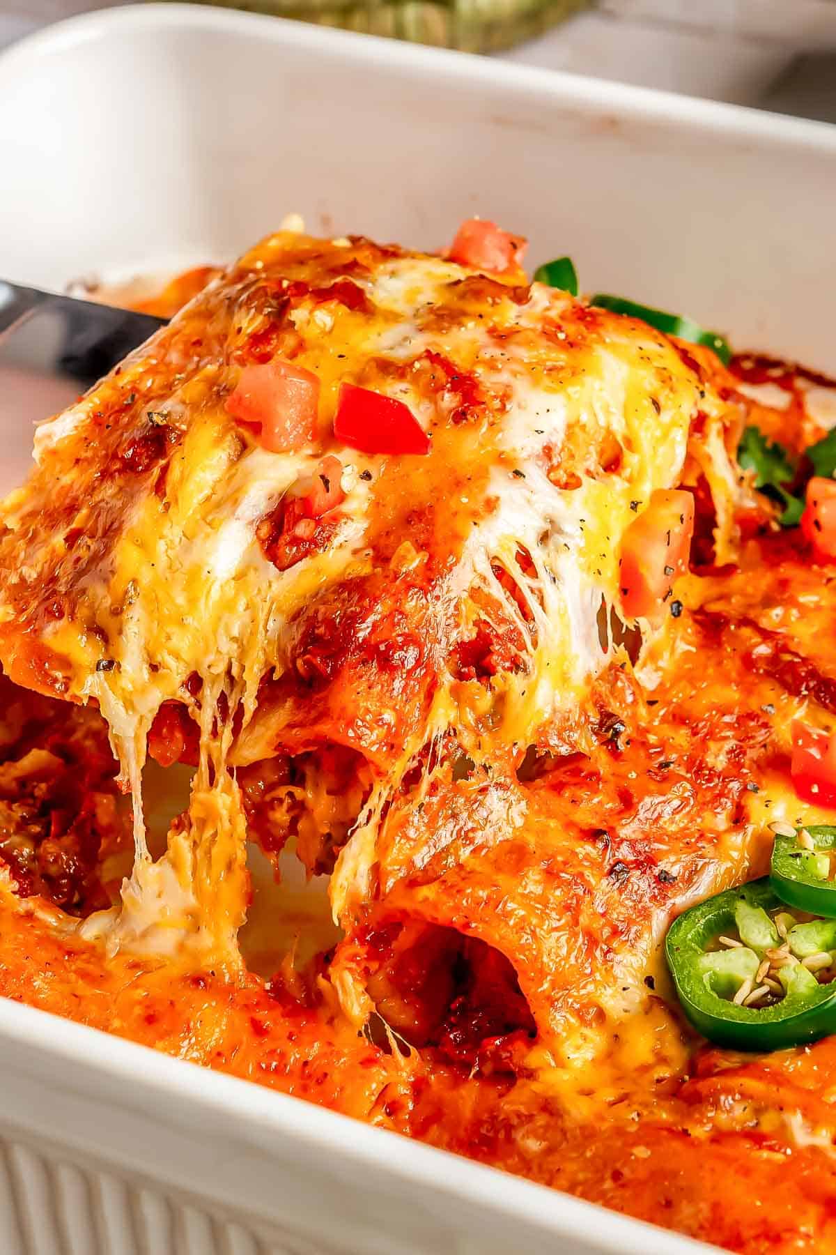 two beef enchiladas being lifted out of a baking dish