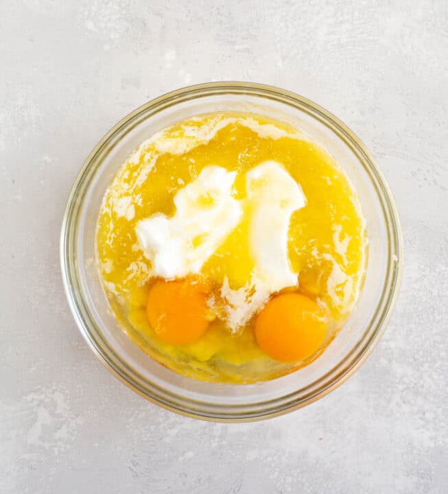 two eggs, yogurt, mashed bananas, melted butter in a clear bowl