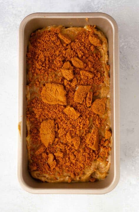crushed biscoff cookies sprinkled on top of batter in a metal loaf pan