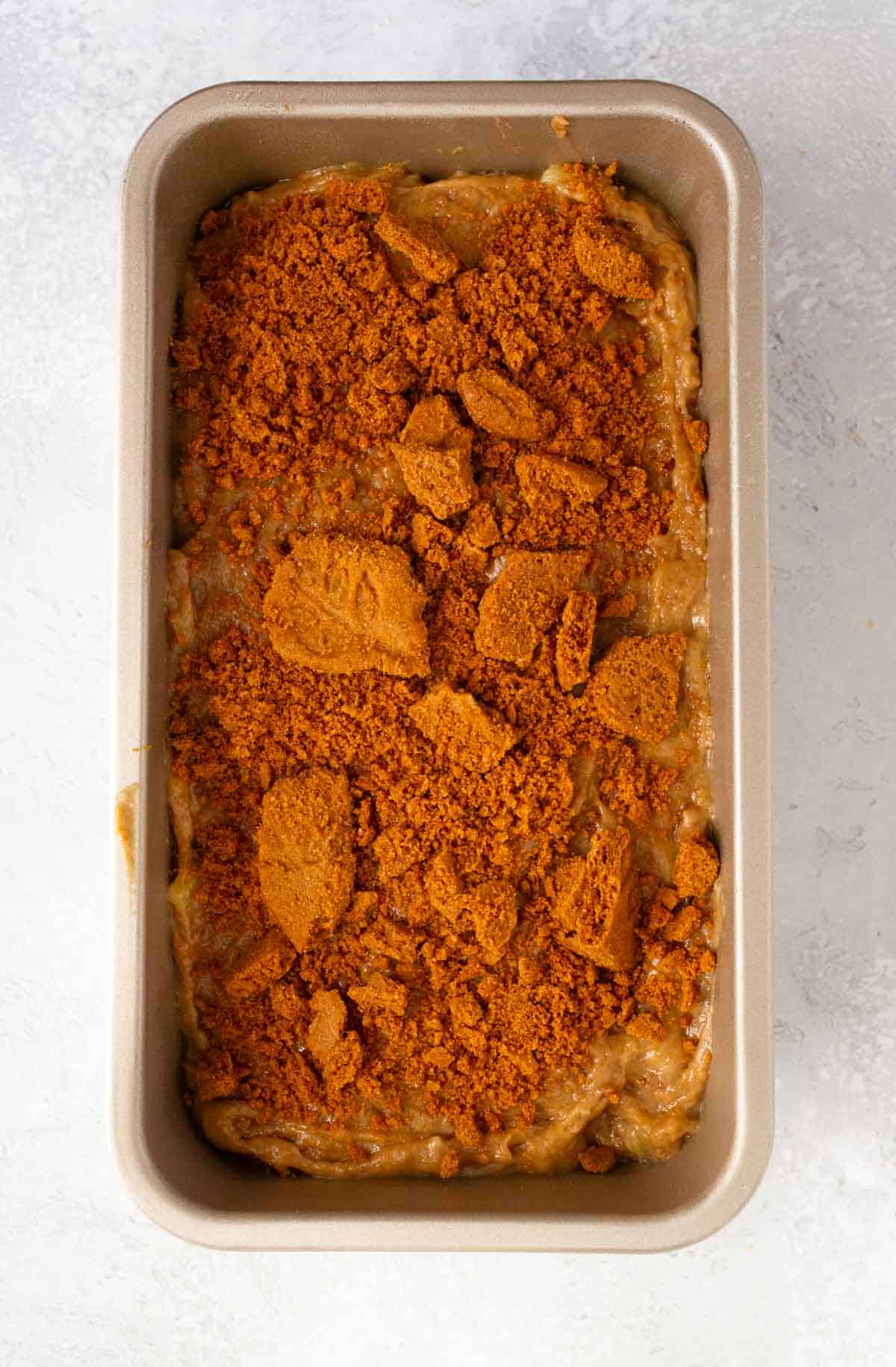 crushed biscoff cookies sprinkled on top of batter in a metal loaf pan