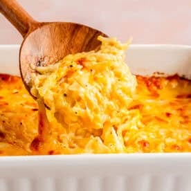 a wooden spoon scoops out cheesy hashbrown casserole from the baking dish