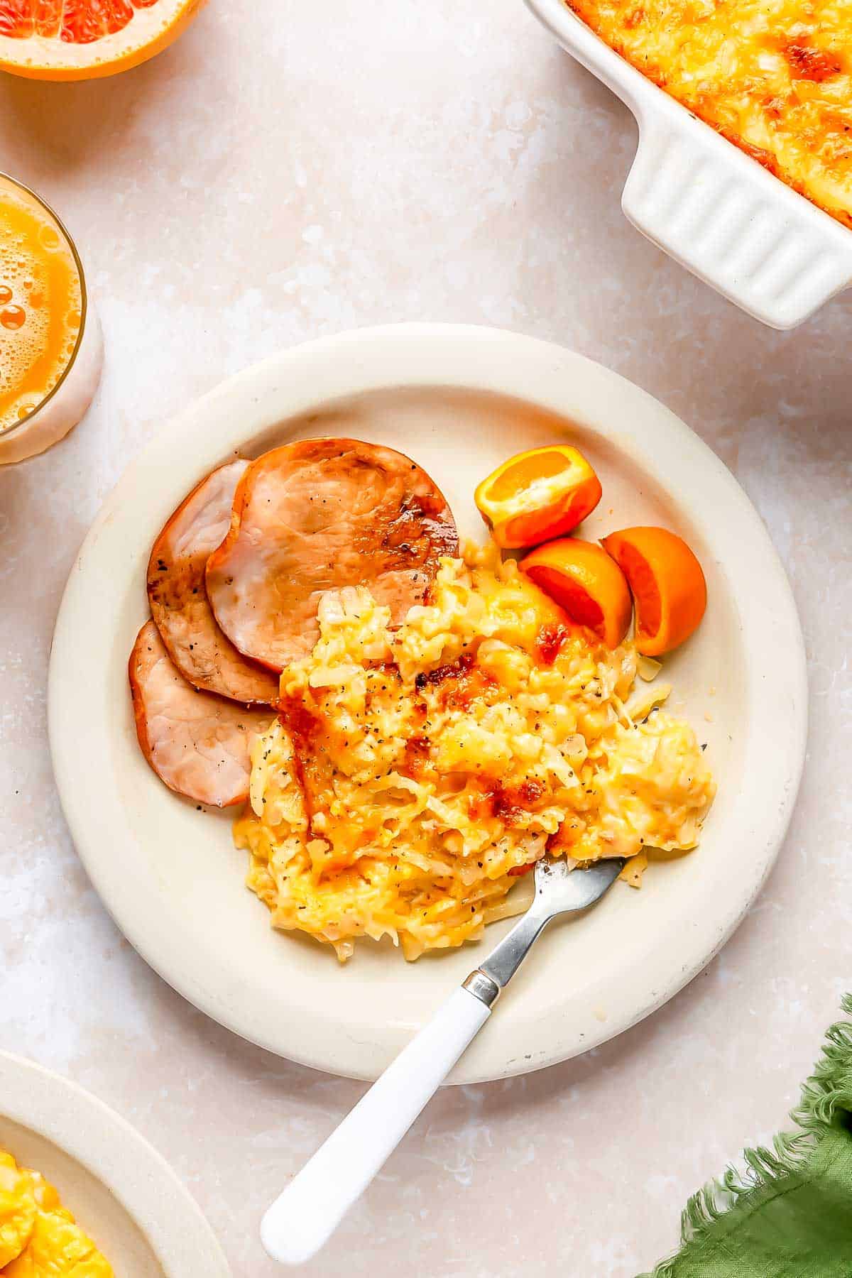 cheesy hashbrowns plated with canadian bacon and orange slices