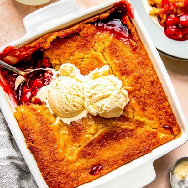 cherry cobbler with two scoops of vanilla ice cream in a square baking dish with a corner spooned out