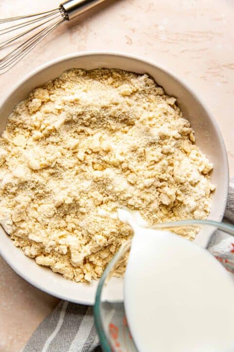 milk is poured into a bowl with butter pieces and flour