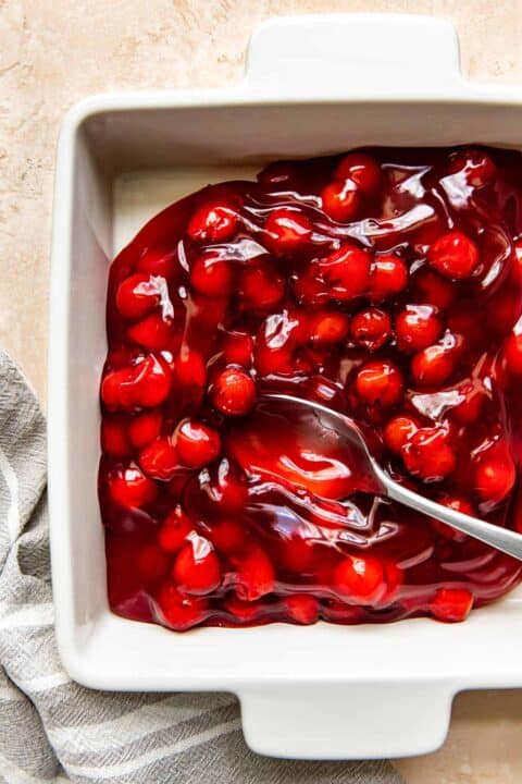 cherry pie filling being spread into a square baking dish