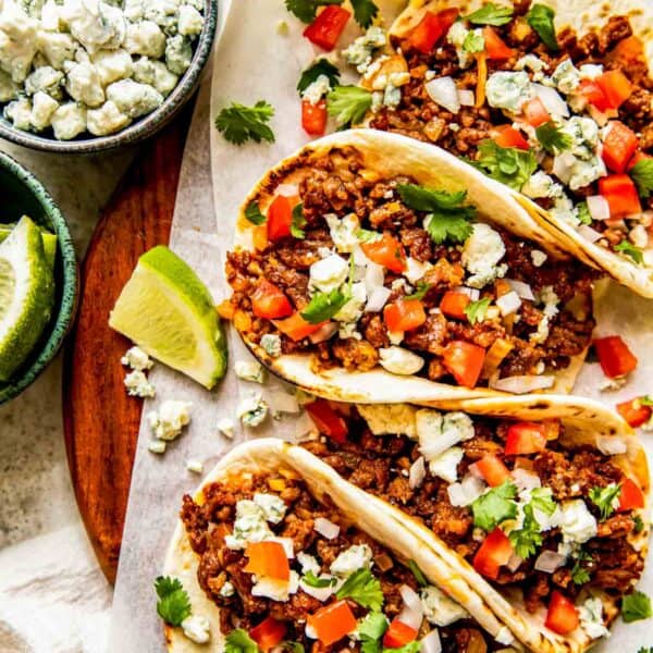 four chorizo tacos on parchment paper next to lime and beer and a bowl of crumbled blue cheese