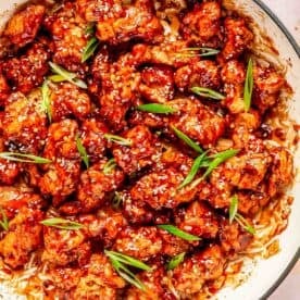 general tso's chicken in a cast iron skillet topped with white sesame seeds and fresh scallions