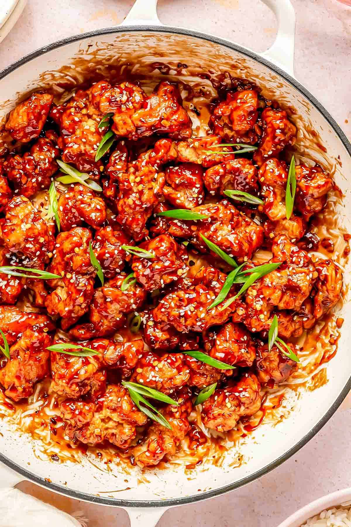 general tso's chicken in a cast iron skillet topped with white sesame seeds and fresh scallions