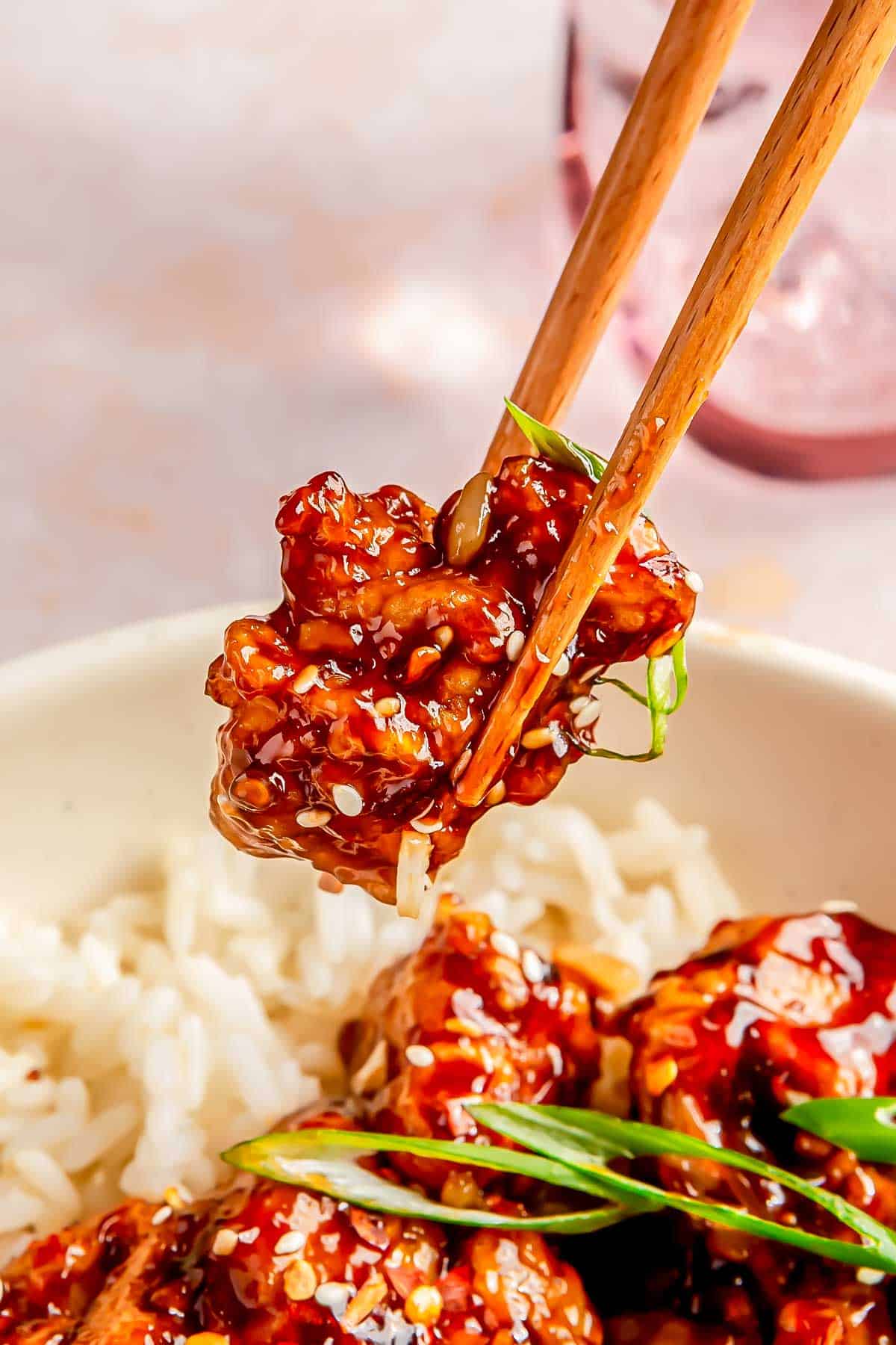 a pair of wooden chopsticks holding a piece of saucy general tso's chicken