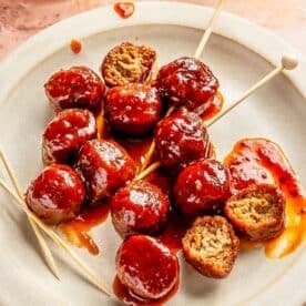 grape jelly meatballs on a white plate with toothpicks throughout them