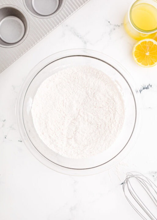 flour and other dry ingredients in a large clear bowl next to a metal whisk